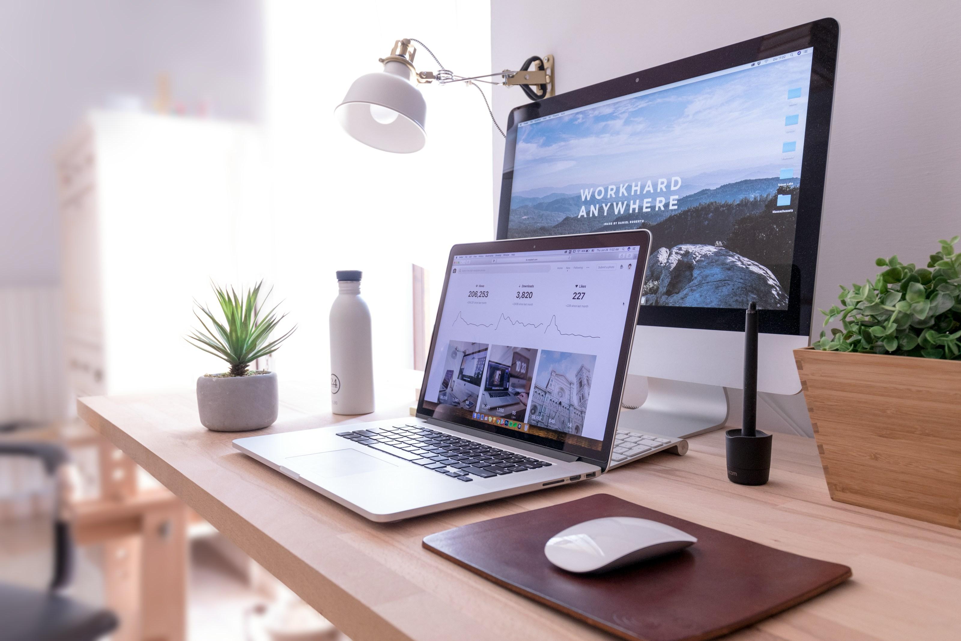 A tidy desk with a laptop and monitor by a window